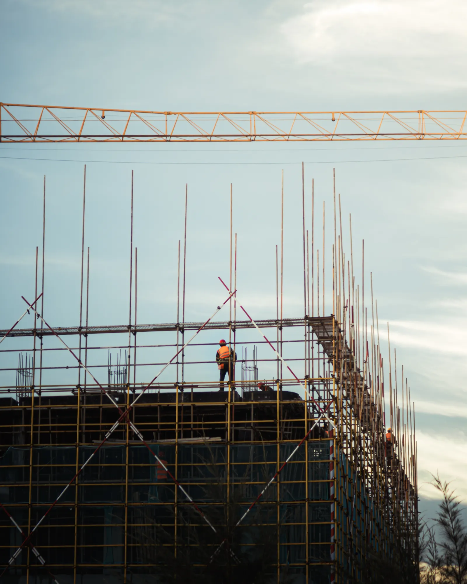 Trabajador de la construcción en lo alto de un andamio junto a una grúa, contra el cielo